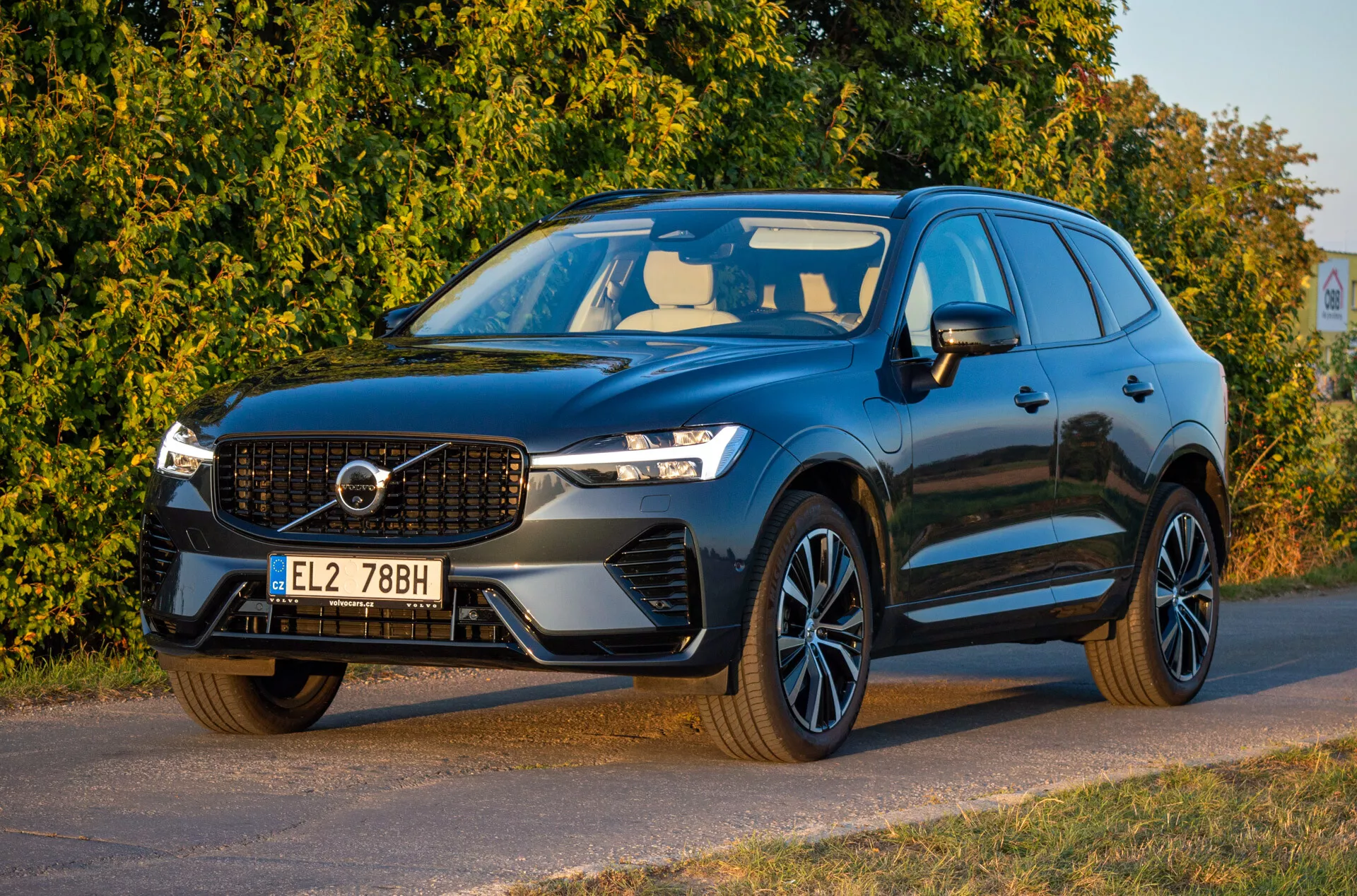 Volvo XC60 Recharge plug-in hibrid iz leta 2021 v temni barvi, pogled spredaj s treh četrtin, ki prikazuje LED žaromete, emblematsko masko, športna platišča in aerodinamično obliko, parkirano diagonalno obrnjeno v levo s podrobnim pogledom na sprednji del in stran voznika.