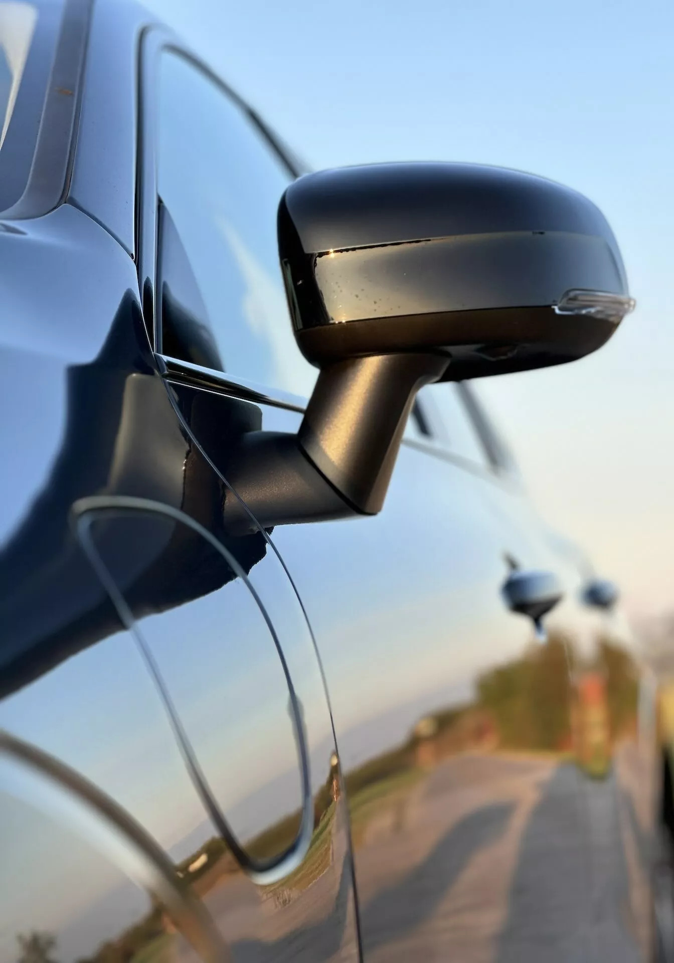 Podroben pogled na stransko ogledalo Volvo XC60 Recharge Plug-In Hybrid 2021, ki prikazuje njegov eleganten dizajn, integriran smernik in pritrditev na vrata avtomobila, kar poudarja avtomobilsko tehnologijo in varnostne funkcije.