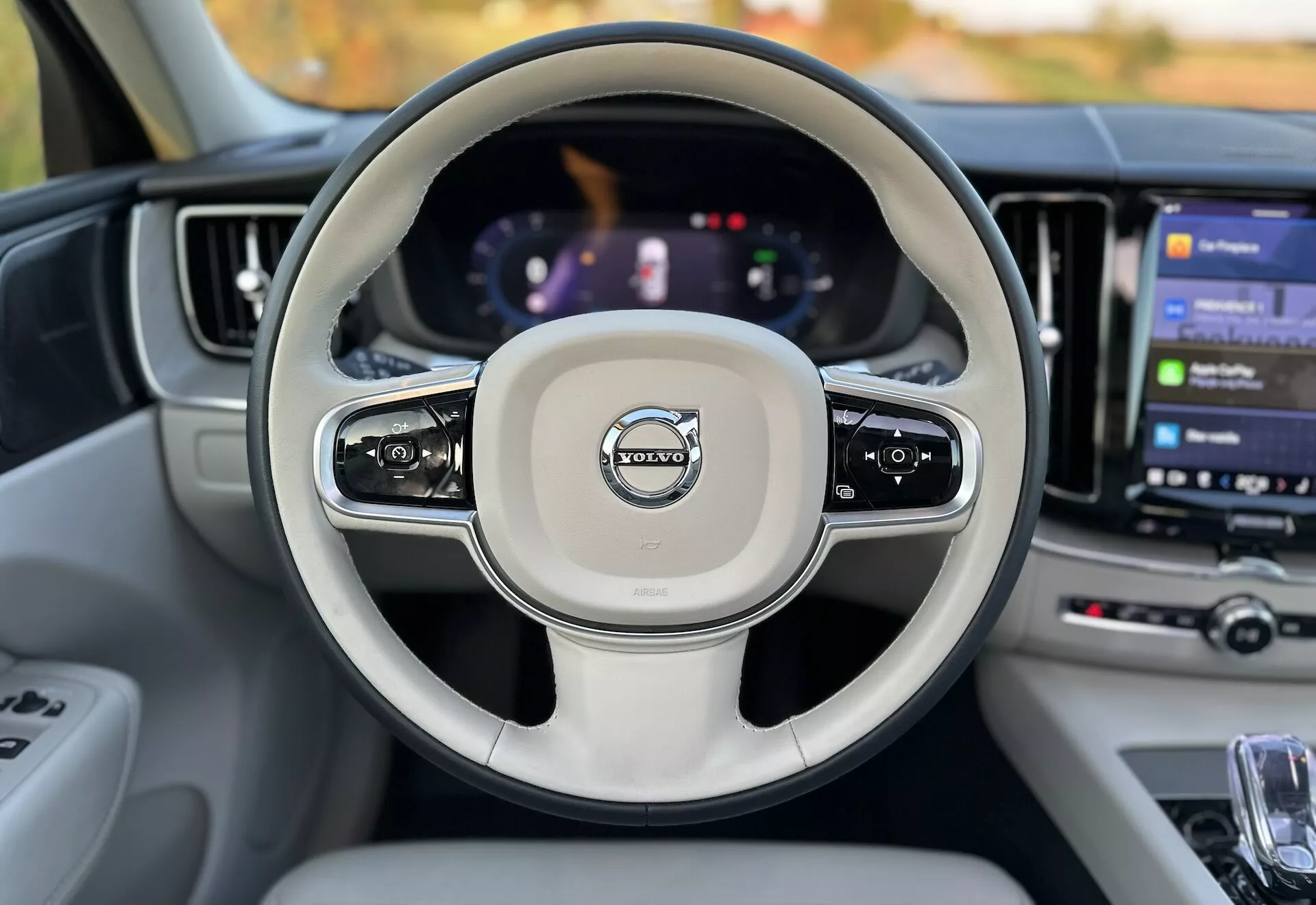 Pogled na notranjost vozila Volvo XC60 Recharge Plug-In Hybrid 2021 iz perspektive voznikovega sedeža, ki prikazuje volan z nameščenimi kontrolami, digitalno instrumentno ploščo in velik zaslon na dotik infotainment sistema