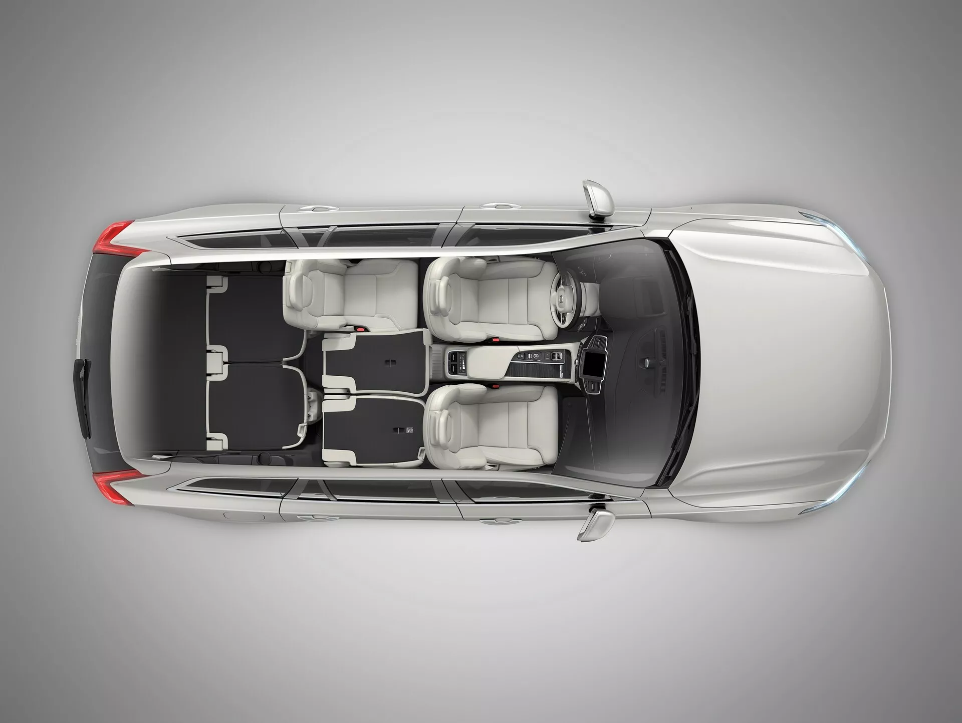 Pogled z vrha na limuzino Volvo XC90 druge generacije iz leta 2015 s prozorno ali digitalno odstranjeno streho, ki prikazuje notranjost. Slika razkriva dolg prednji pokrov avtomobila, štiri zaprta vrata, štiri kolesa in razporeditev sedežev z dvema sprednjima sedežema in zadnjo klopjo za tri potnike. Vidna sta osrednja konzola in prestavna ročica. Pokazano je levo krmilo z volanom, zaslonom in razporeditvijo nadzora na armaturni plošči. Oblikovalski elementi, kot so vzglavniki, zunanja ogledala in notranji prostor ter razporeditev so jasno vidni.