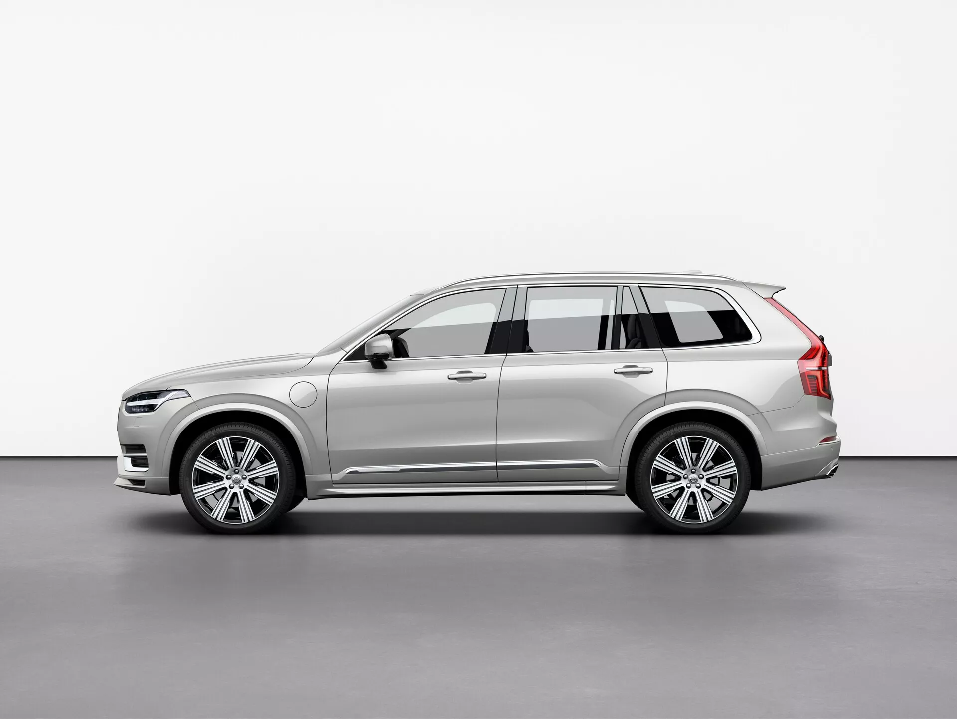 Slika SUV Volvo XC90 2015, fotografirana iz tretjega kota z rahlim kotom. Ta pogled poudarja tako sprednje kot bočne profile, ki prikazujejo eleganten in moden dizajn avtomobila, zapletene LED žaromete, delno vidno sprednjo masko, večkraka platišča iz aluminijeve zlitine, stranska ogledala z integriranimi smerniki, strešne nosilce, dinamične linije karoserije, barvo in barvo avtomobila. Mehka osvetlitev v studijskem okolju natančno odraža obrise in površinske detajle vozila.
