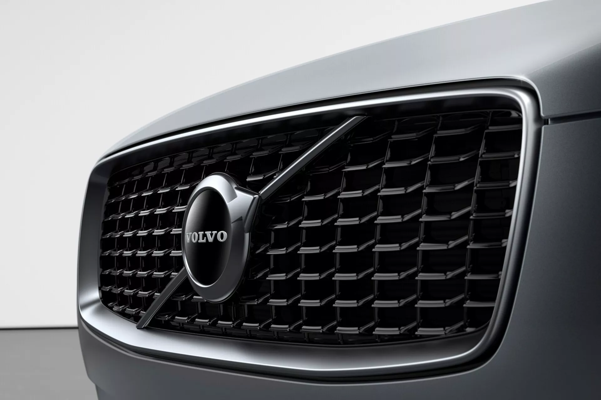 Bližnji pogled na sprednjo masko Volva XC90 2015 (2. generacija), ki prikazuje podroben dizajn in izrazit Volvo znak. Maska ima navpične lamele in kromiran obris, kar poudarja razkošje in sodobno estetiko.