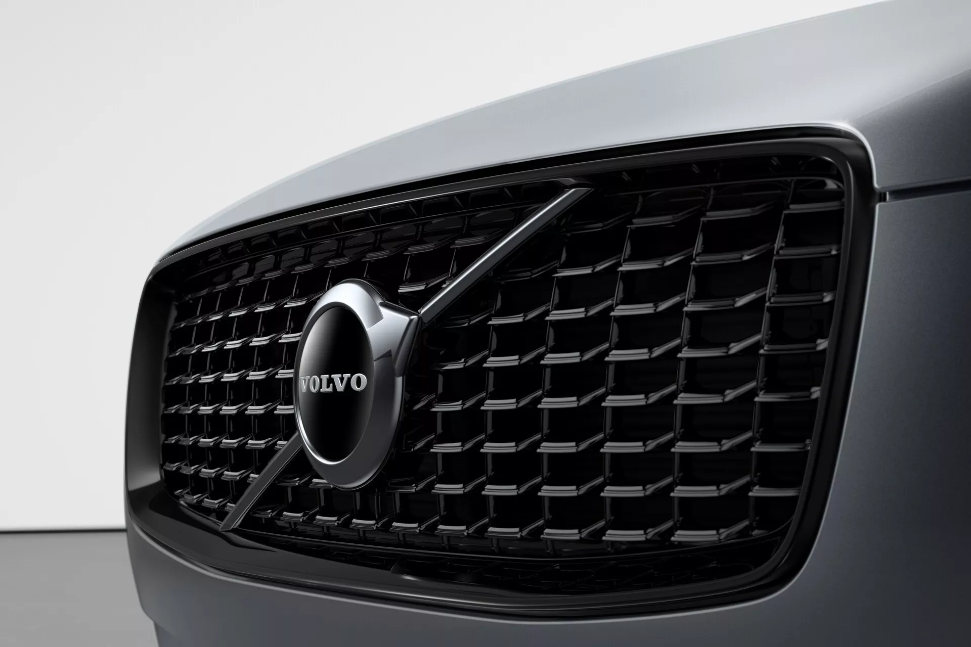 Bližnji pogled na prednjo masko Volvo XC90 2015 z izrazitim Volvo emblemom. Emblem je centriran v maski in je sestavljen iz srebrnega kroga s puščico in napisom 'VOLVO'. Vzorec satovja in elegantni mat okvir poudarjata prefinjeno in sodobno zasnovo.