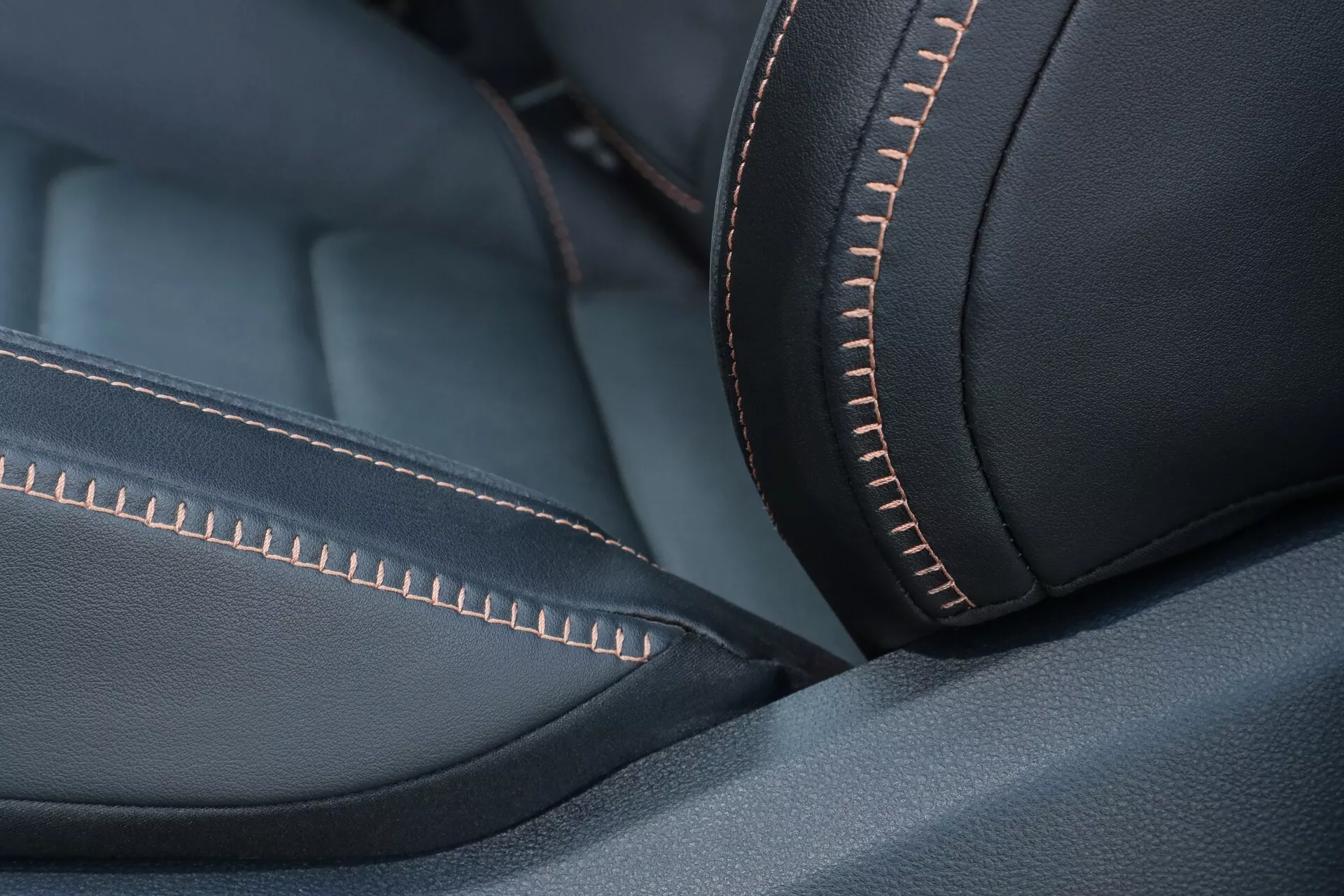 Podroben posnetek usnjene oblazinjene notranjosti VW Nutzfahrzeuge Amarok 2023 (2. generacija), ki prikazuje visokokakovosten material z gladko teksturo in mat zaključkom. Izraziti, natančni oranžni šivi dodajajo kontrastno barvo niti, poudarjajoč dizajn in estetiko. Poševni kot poudarja ukrivljenost in ergonomsko udobje sedeža. Plitka globinska ostrina ostro izostri šive, medtem ko se preostanek nežno zamegli. Mehka, razpršena osvetlitev izboljša kakovost materiala brez ostrih odsevov. Temni toni in oranžni kontrast ustvarjajo minimalističen, eleganten vtis, ki nakazuje luksuz in visoko kakovost izdelave.
