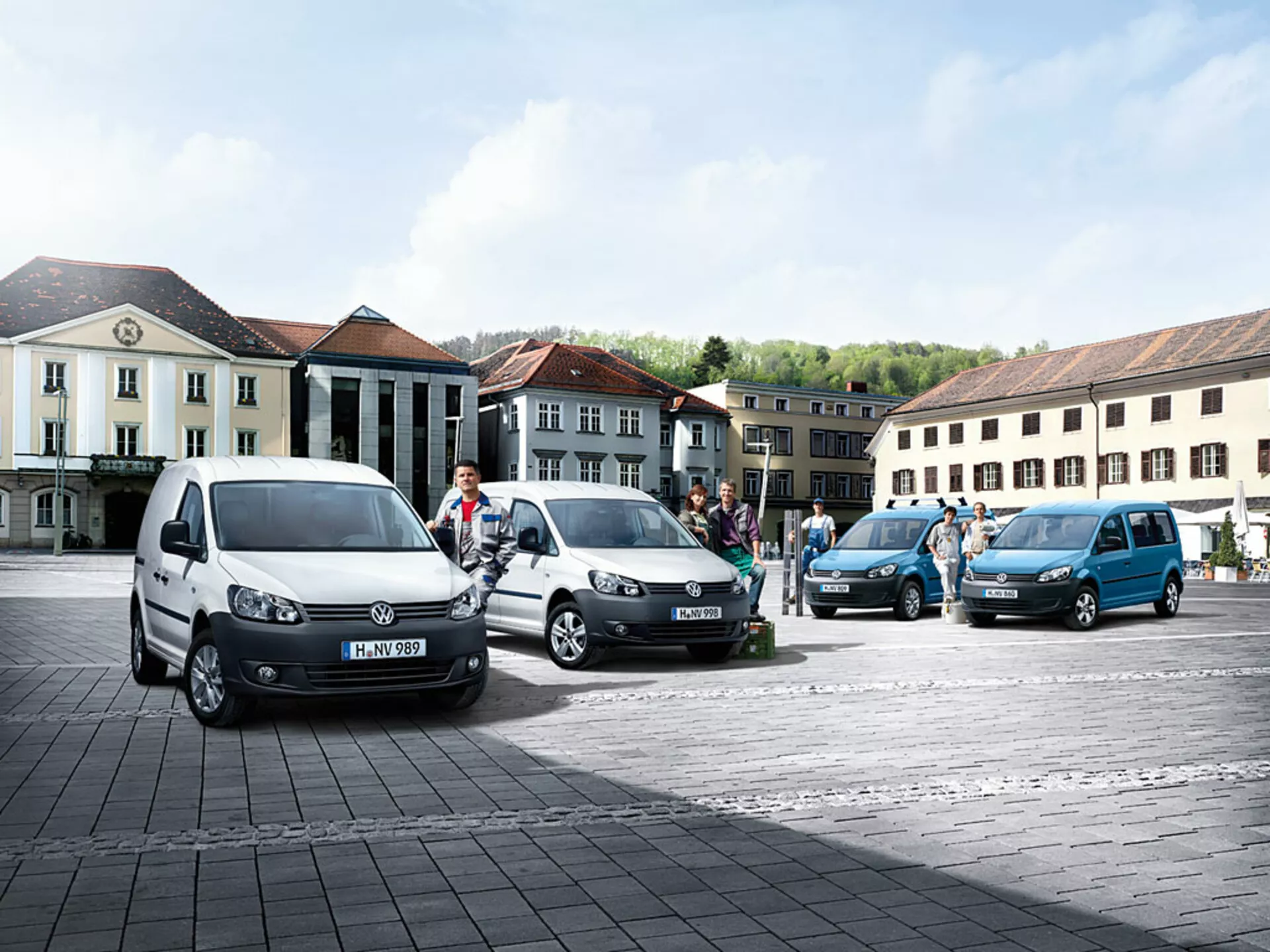 Večnamenski kombiji Volkswagen Caddy 2010 parkirani v diagonalni liniji na tlakovanih trgih, prikazujejo različne barve in kote, z vidnimi značilnimi profili spredaj in ob strani