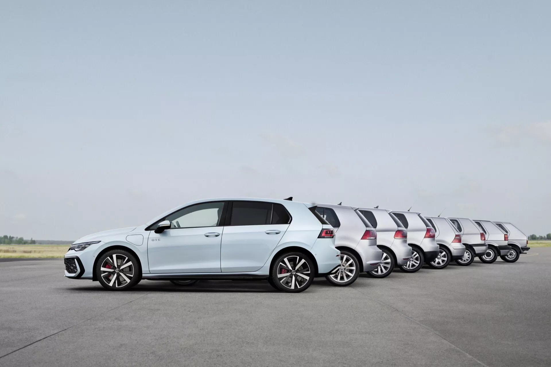 VW Golf Hatchback 2024 (VIII-Facelift) v trdni beli barvi, prikazuje gibanje preko efekta časovnega zamika na vzletno-pristajalni stezi, značilnosti vključujejo obliko hatchback, platišča iz zlitine, integrirane smerne kazalnike v barvanih stranskih ogledalih in kontrastno črno streho.
