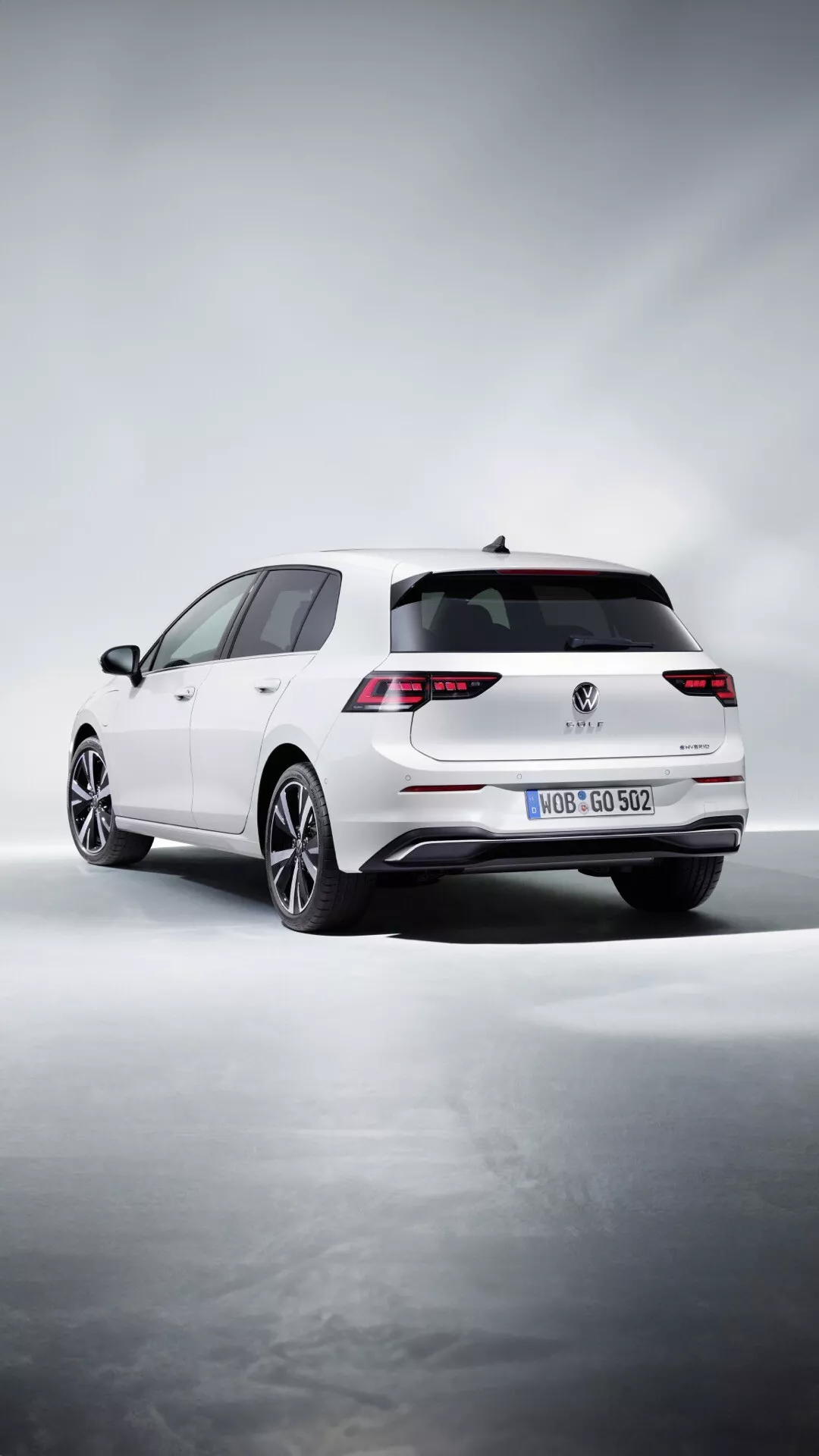 Bel hatchback Volkswagen Golf (VIII Facelift) letnik 2024, perspektiva s treh četrtin zadaj prikazuje LED zadnje luči, dvojne izpušne cevi, večkraka lita kolesa in zadnji strešni spojler na stiliziranem studijskem ozadju