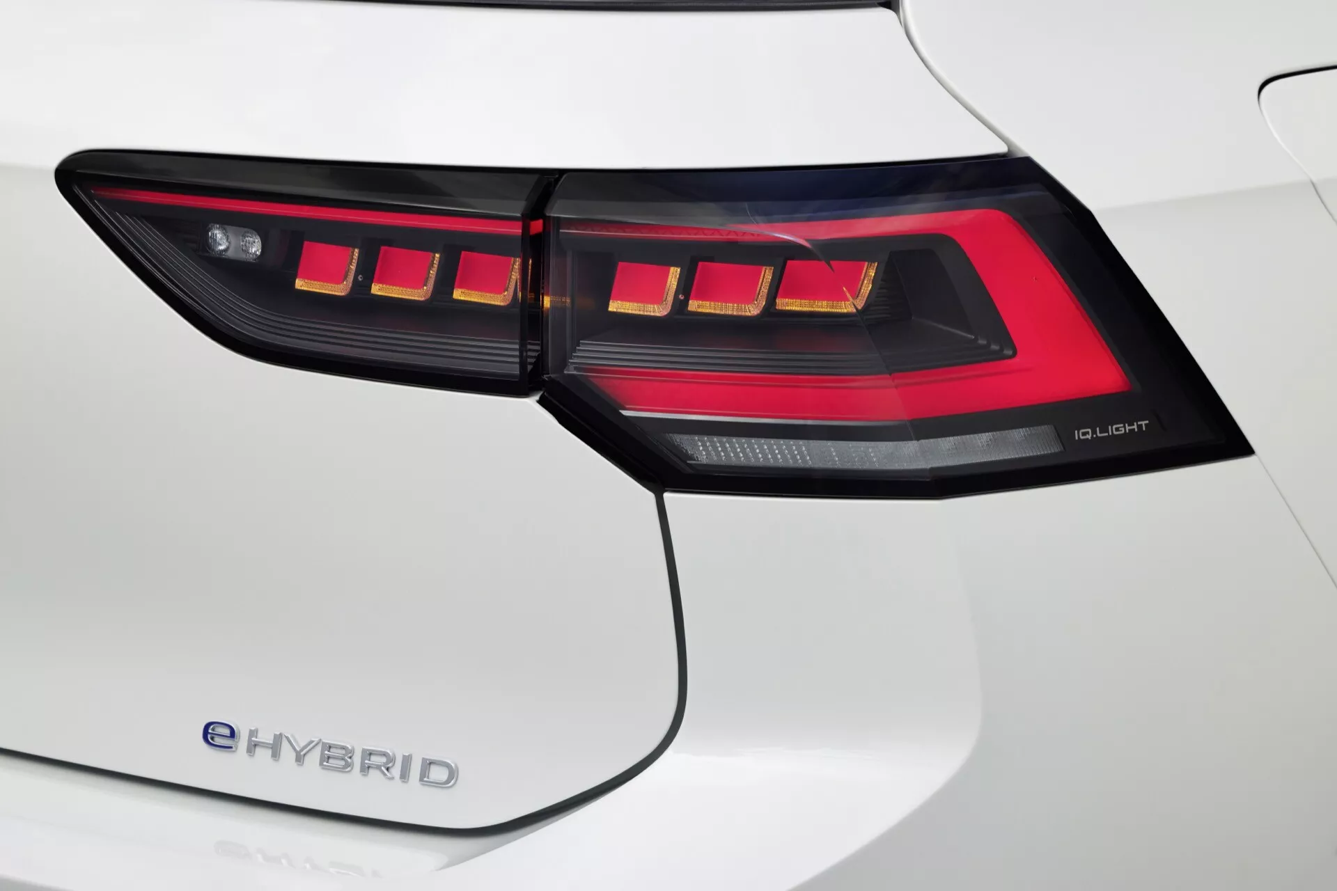 Pogled od blizu na zadnjo luč na desni strani VW Golfa 2024 (VIII facelift) e-HYBRID z OLED tehnologijo in izrazitim LED vzorcem, dopolnjen z belo zadnjo četrtino karoserije.