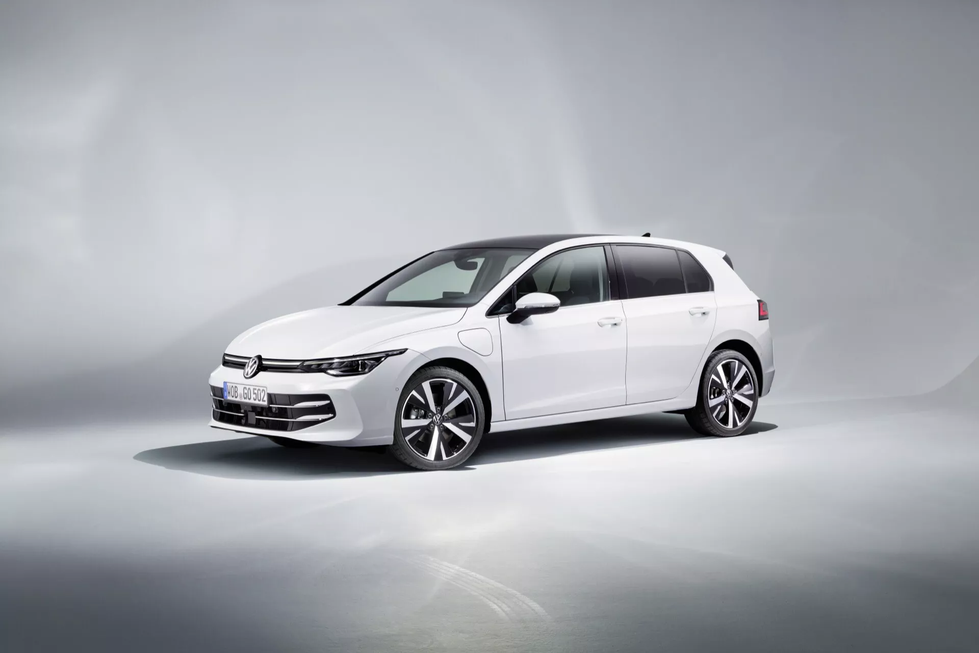 VW Golf (VIII-Facelift) 2024 v beli barvi, prikazuje dinamičen tričetrtinski sprednji pogled na odsevni površini z gradientnim ozadjem, poudarjajoč njegove tanke LED dnevne luči, vodoravno masko, večkraka lita platišča, stranska ogledala z integriranimi smerokazi in zatemnjena okna.