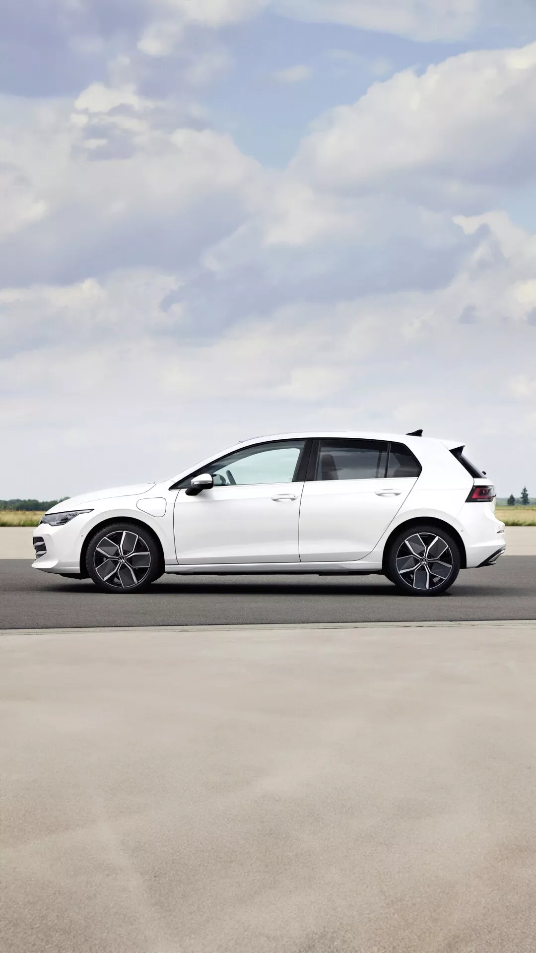 Bočni pogled na Volkswagen Golf VIII Facelift 2024 s športnimi litoimi kolesi, padajočo streho in belo barvno dokončavo na jasen dan na prostem