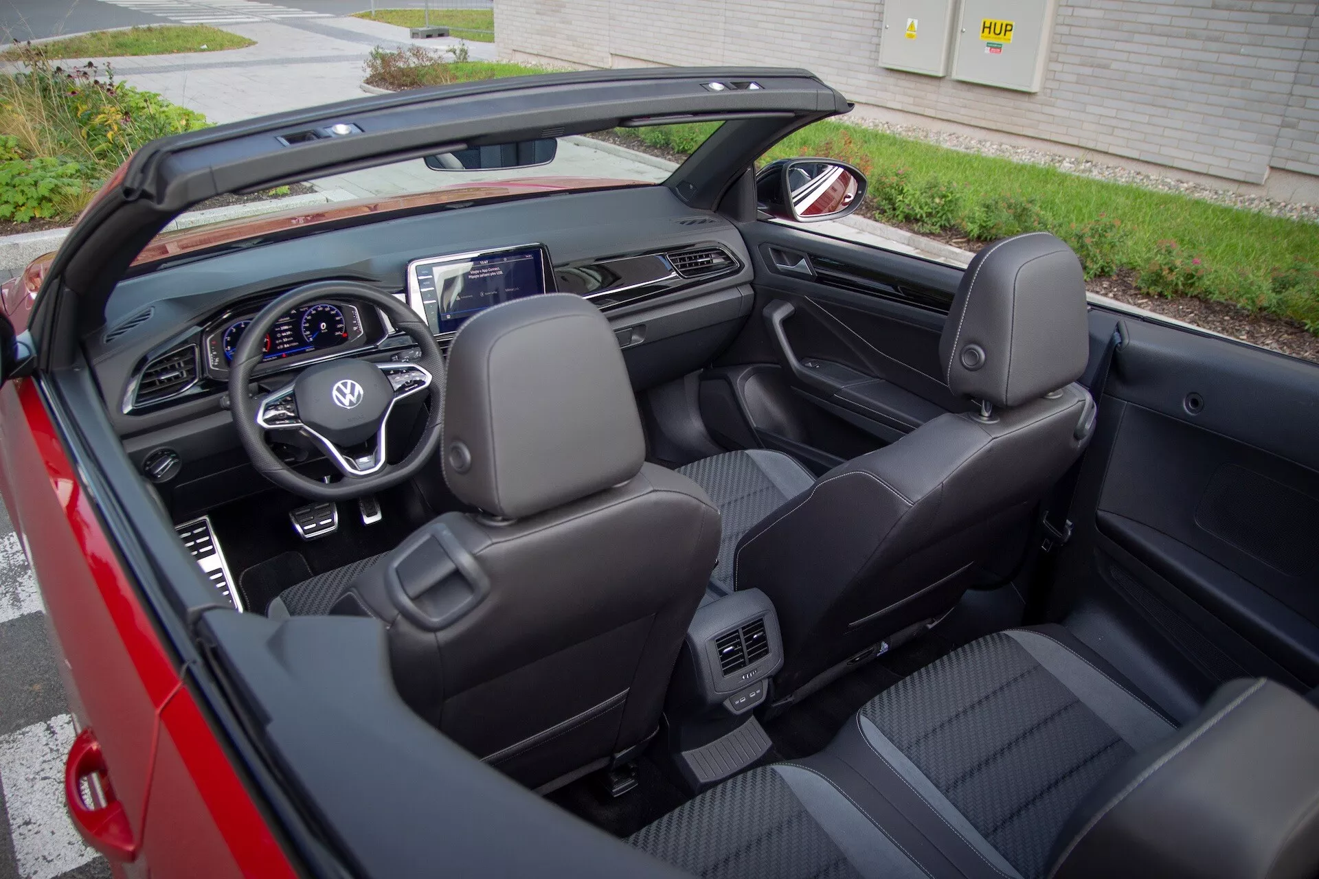 Pogled na notranjost kabrioleta VW T-Roc Cabriolet 2022 s spuščeno streho, črna usnjena sedeža, multifunkcijski volan, digitalna armaturna plošča in centralni zaslon za infotainment iz rahlo desnega kota od zgoraj