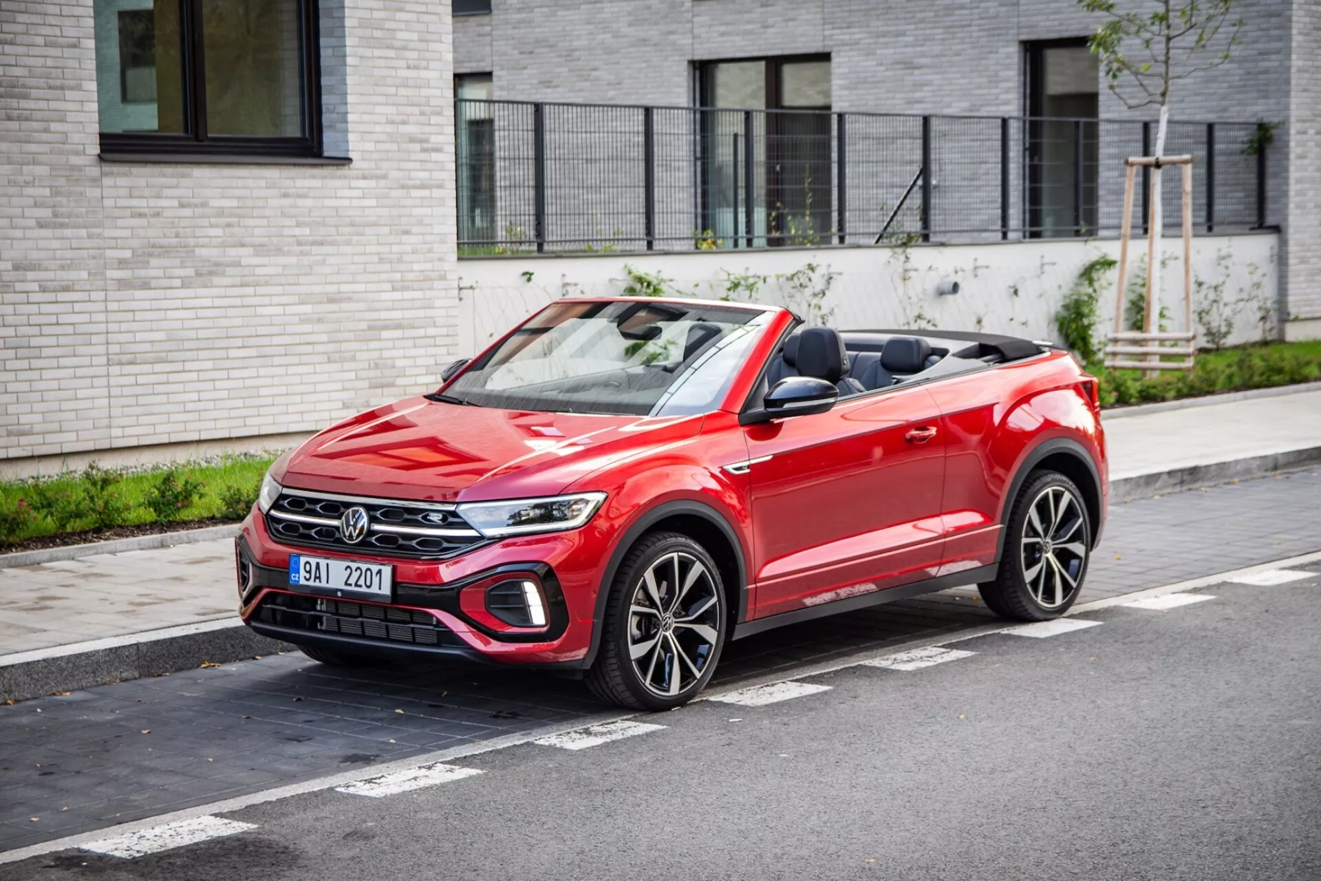 VW T-Roc Cabriolet 2022 parkiran na mestni ulici prikazuje sprednjo masko, LED žaromete, zloženo platneno streho in športna večkraka kolesa