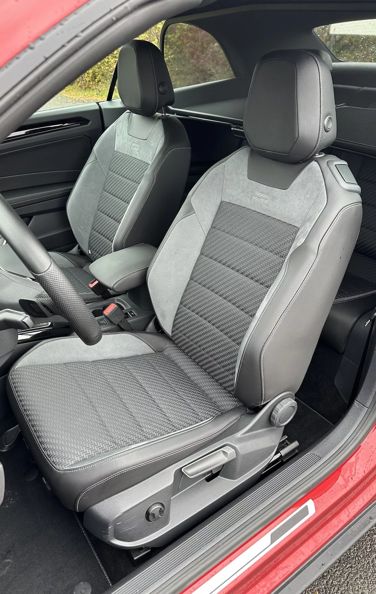 Pogled na notranjost kabrioleta VW T-Roc 2022 s poudarkom na sprednjih sedežih voznika in sopotnika, oblazinjenih z dvobarvno tkanino, ki prikazuje nastavljive vzglavnike, ročne nastavitvene kontrole sedeža in izrazite bočne ojačitve za izboljšano podporo.