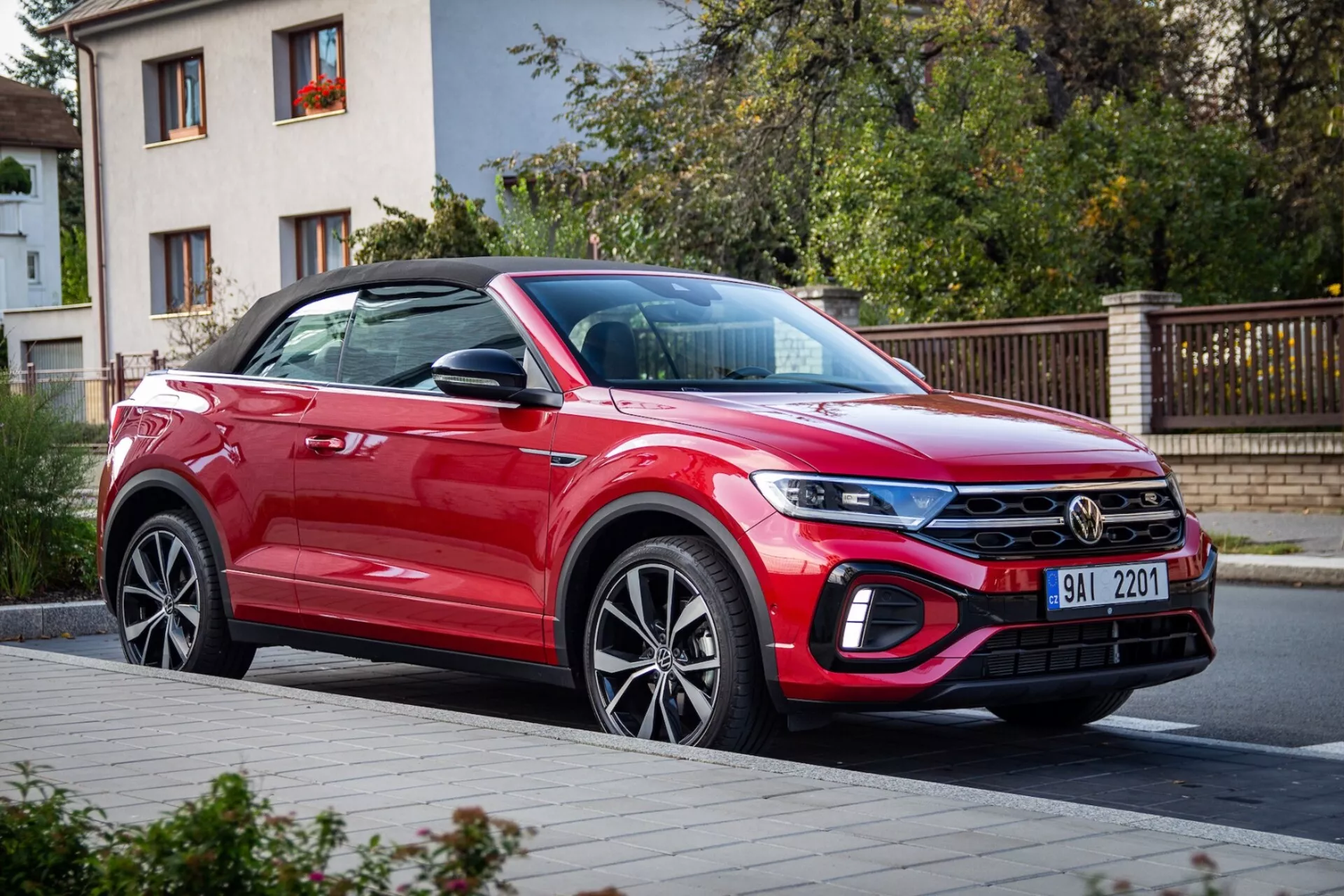 VW T-Roc Cabriolet 2022 v rdeči barvi, ki prikazuje sodobno oblikovanje kompaktnega SUV-ja s poudarkom na sprednjem blatniku, LED žarometih, rešetki z kromirano palico, sprednjem odbijaču z možnimi adaptivnimi značilnostmi, vratih sopotnika in platiščih iz zlitine, parkiranem na mestni ulici.
