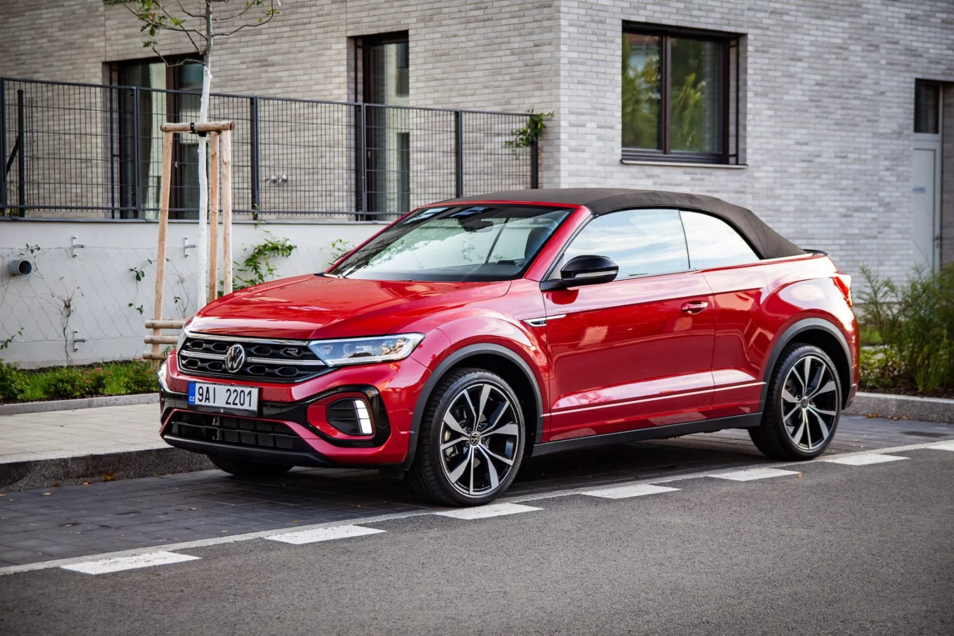 Svetlo rdeč kabriolet crossover SUV VW T-Roc 2022 parkiran ob robu ceste, prikazuje sprednjo masko, LED žaromete, lita platišča in mehko streho, v treh-četrtinskem sprednjem pogledu v jasnem vremenu