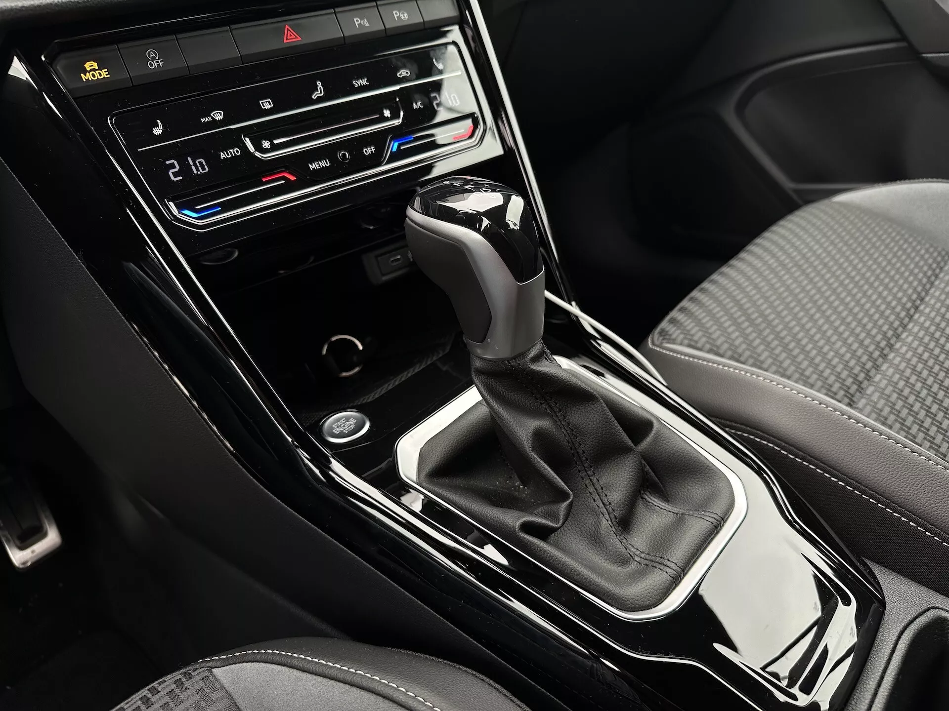 Podroben pogled na sredinsko konzolo VW T-Roc Cabriolet 2022 z avtomatskim menjalnikom, dvopodročnim klimatskim nadzorom, gumbi za ogrevanje in prezračevanje sedežev ter nadzornim zaslonom