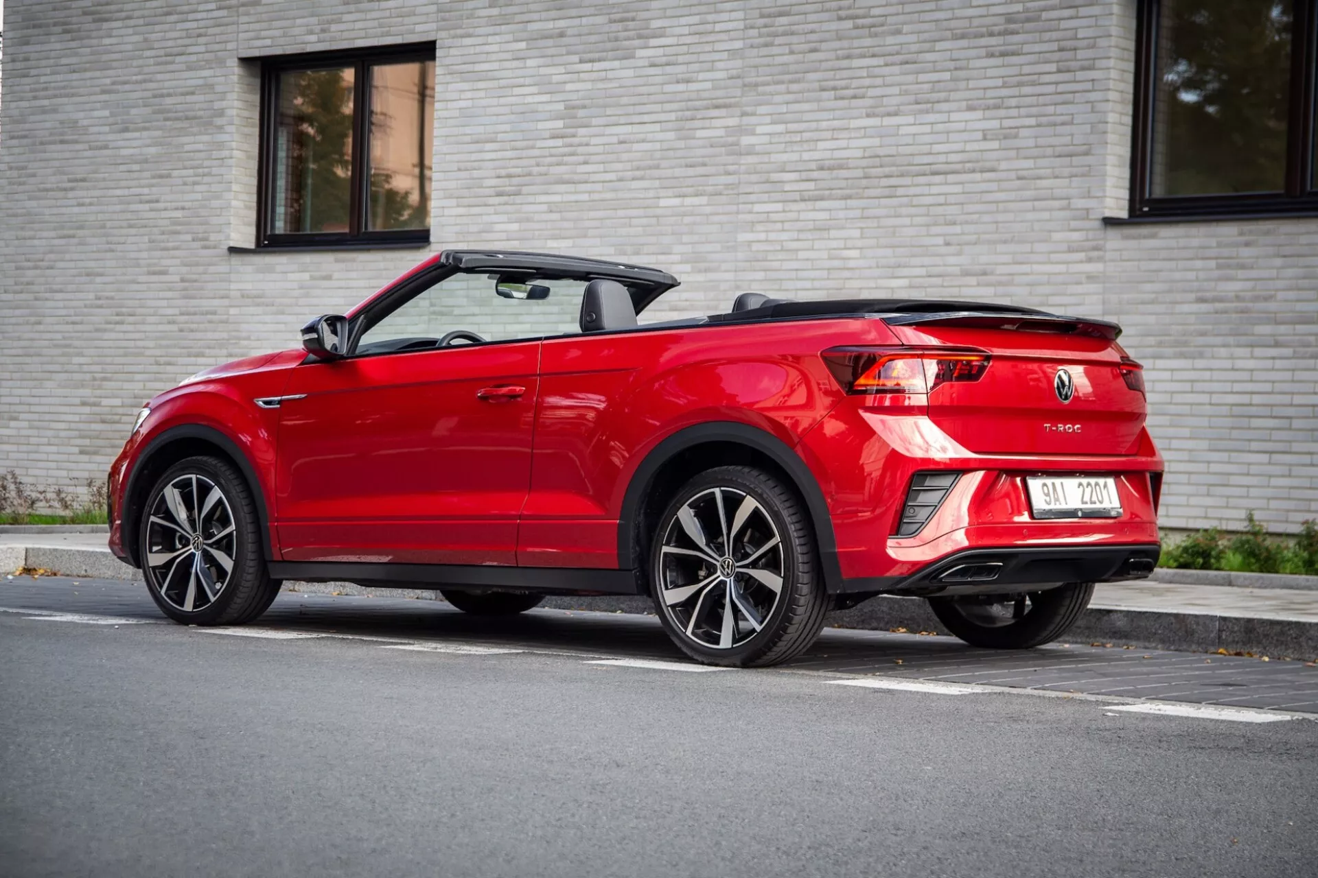 Trčetrtinski zadnji pogled na rdeči VW T-Roc Cabriolet iz leta 2022 s spuščeno mehko streho, ki prikazuje LED zadnje luči, dvojne izpuhe in večkraka lita kolesa, parkiran na ulici pod mehko dnevno svetlobo